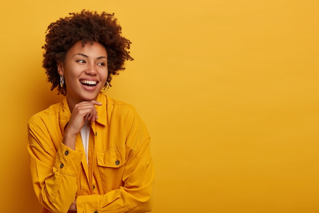 Mujer africana con belleza natural, expresión despreocupada, mira a un lado, tiene actitud amistosa feliz