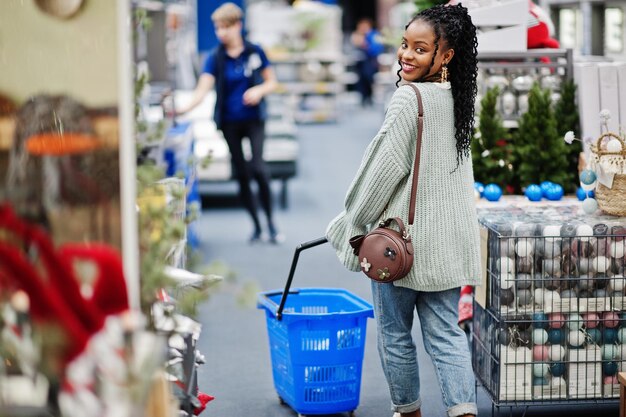 Mujer africana caminando con cesta de la compra en una tienda de muebles para el hogar moderno