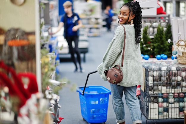 Mujer africana caminando con cesta de la compra en una tienda de muebles para el hogar moderno