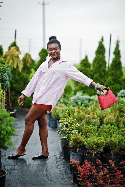 Mujer africana con camisa rosa grande posada en el jardín con plántulas