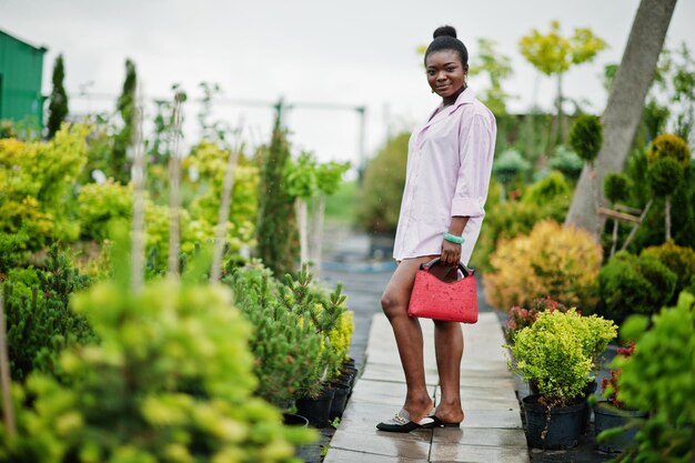 Mujer africana con camisa rosa grande posada en el jardín con plántulas