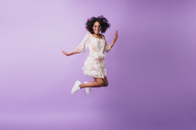 Mujer africana delgada en zapatillas blancas saltando y riendo. Foto interior de una chica negra de buen humor bailando.