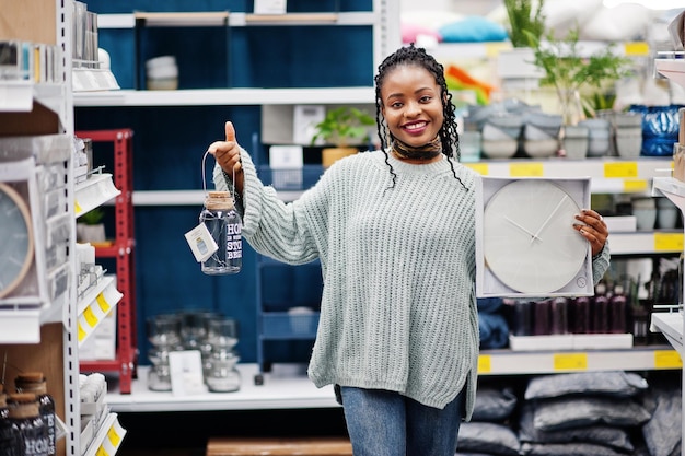 Mujer africana eligiendo reloj para su apartamento en una moderna tienda de muebles para el hogar