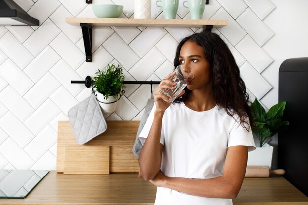 Mujer africana se encuentra en la cocina y bebe agua