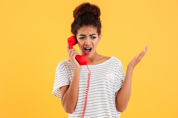 Mujer africana enojada gritando mientras habla por teléfono rojo