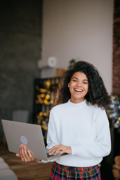 Mujer africana feliz joven que sostiene la computadora portátil en las manos