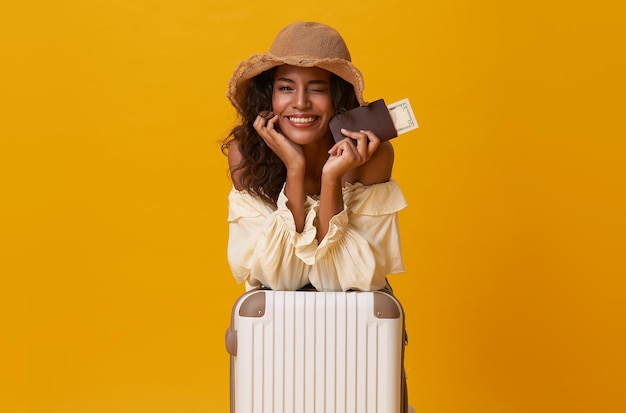 Mujer africana feliz sentada con maleta aislada de fondo amarillo