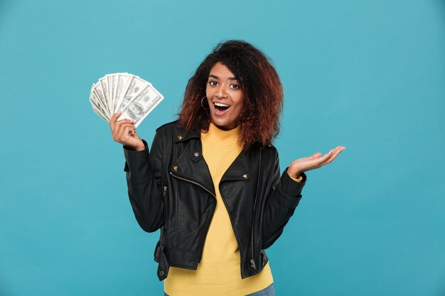 Mujer africana feliz sorprendida en chaqueta de cuero con dinero