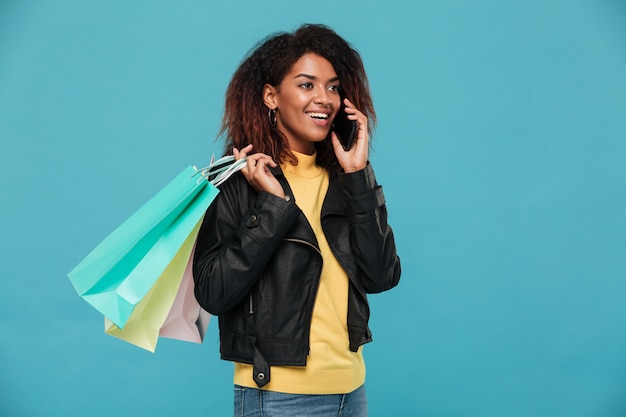 Mujer africana feliz sosteniendo bolsas de compras hablando por teléfono.