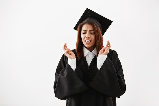 Mujer africana graduada en manto negro rezando sobre superficie blanca