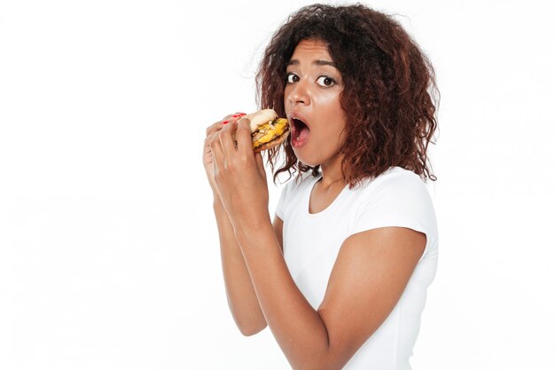 Mujer africana joven confundida comiendo hamburguesa.