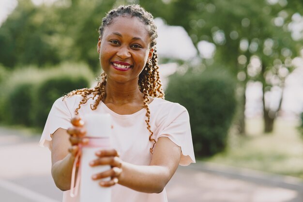 Mujer africana joven sana al aire libre en la mañana. Chica con botella de agua.