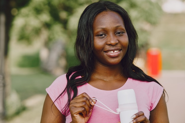 Mujer africana joven sana al aire libre en la mañana. Chica con botella de agua.