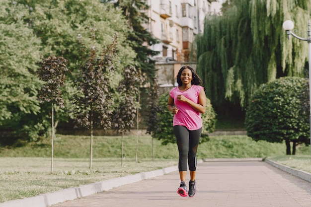 Mujer africana joven sana al aire libre en la mañana. Mujer en camiseta rosa.