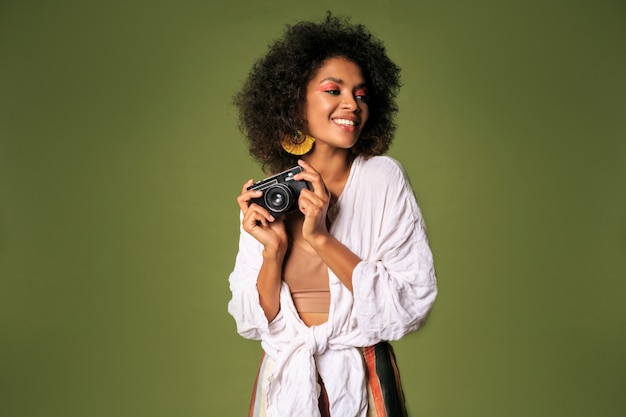 Mujer africana con maquillaje brillante sosteniendo cámara de fotos retro y riendo.