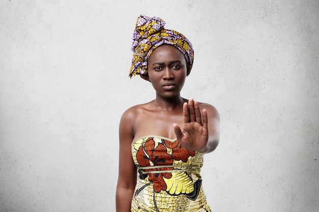 Foto gratuita ¡para! mujer africana de piel oscura y lisa con ropas tradicionales mostrando su palma negando no hacer algo. mujer de piel oscura confiada que no muestra ningún gesto. concepto de veto y demanda