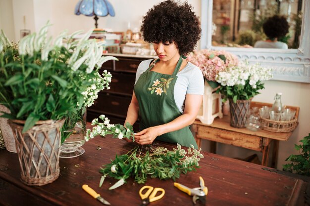 Mujer africana que clasifica las plantas de la flor en el escritorio de madera