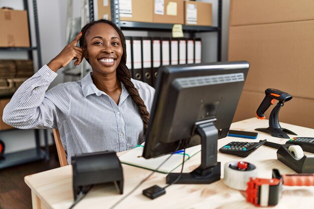 Mujer africana que trabaja en el comercio electrónico de pequeñas empresas sonriendo apuntando a la cabeza con un dedo, gran idea o pensamiento, buena memoria