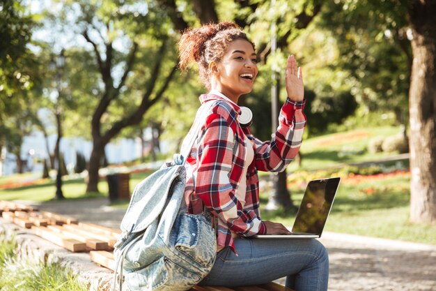 Mujer africana sentada al aire libre en el parque con ordenador portátil.