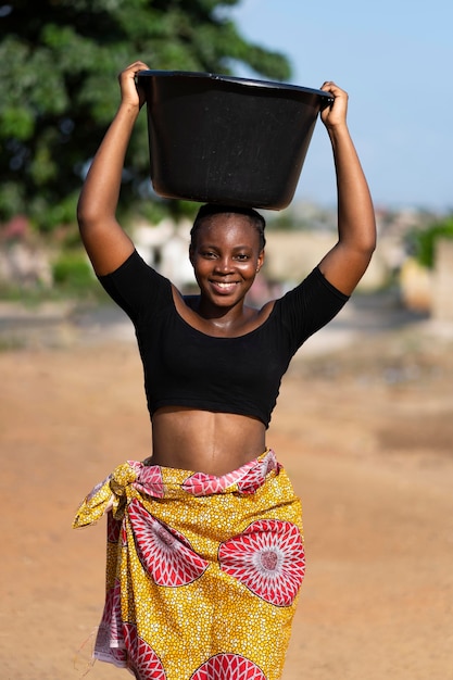 Mujer africana, teniendo, un, balde de agua, en, ella, cabeza