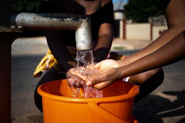 Mujer africana vertiendo agua en un recipiente al aire libre