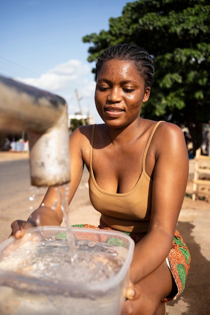 Foto gratuita mujer africana vertiendo agua en un recipiente