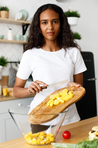 Mujer africana vierte pimiento amarillo cortado en un recipiente de vidrio