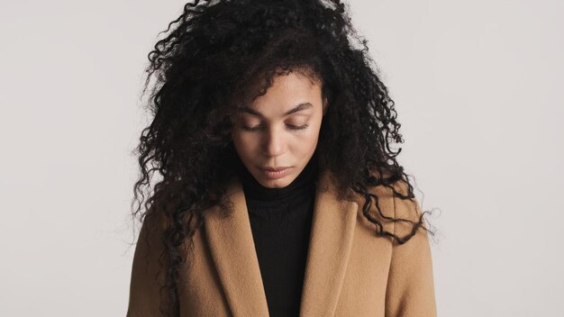 Mujer afro de cabello oscuro vestida con abrigo que parece seria aislada sobre fondo blanco Concepto de expresión facial