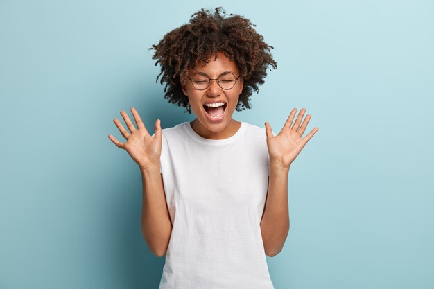 Mujer afro exagerada se ríe a carcajadas, escucha una broma divertida o una historia, levanta las palmas de las manos con satisfacción