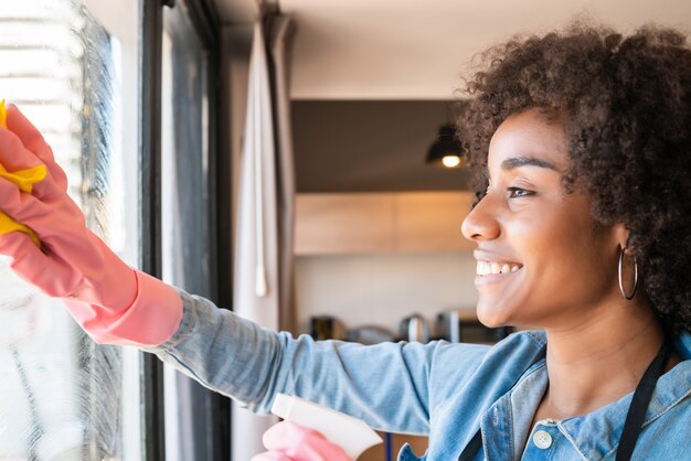 Mujer afro limpieza ventana con un trapo en casa.