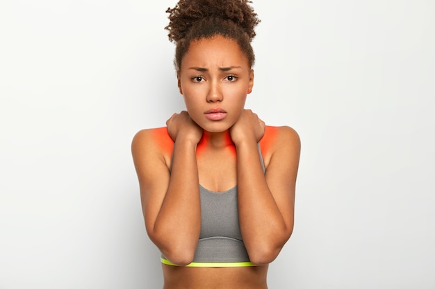 Foto gratuita mujer afro molesta que sufre de dolor de cuello, se ve triste y disgustada, muestra una zona inflamada, vestida con un top informal, tiene la piel oscura