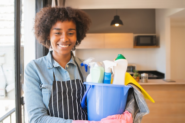 Mujer afro sosteniendo un cubo con artículos de limpieza.