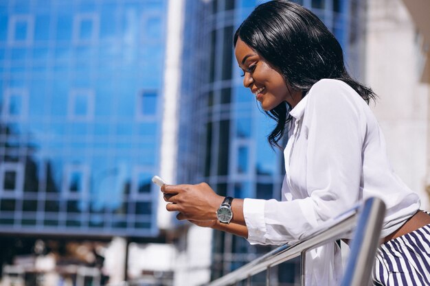 Mujer afroamericana al aire libre por el rascacielos con teléfono