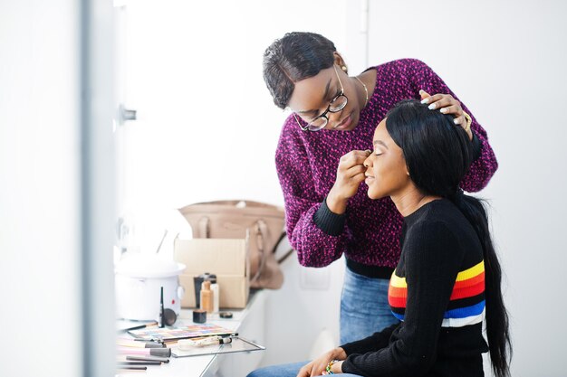 Mujer afroamericana aplicando maquillaje por maquillador en salón de belleza