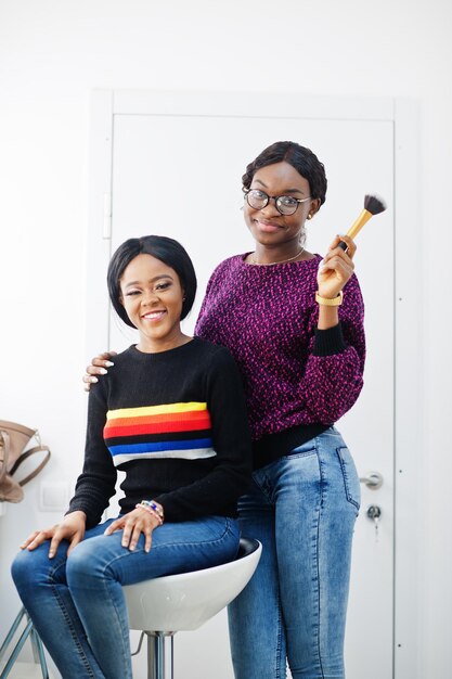 Mujer afroamericana aplicando maquillaje por maquillador en salón de belleza