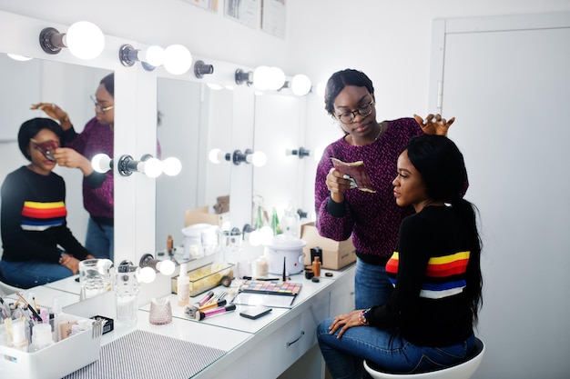 Mujer afroamericana aplicando maquillaje por maquillador en salón de belleza