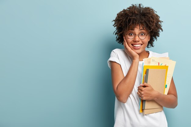 Mujer afroamericana de aspecto agradable tiene cuadernos, papeles, estudios en la universidad, feliz de terminar de estudiar