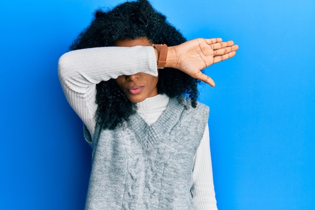 Foto gratuita mujer afroamericana con cabello afro que usa un suéter de invierno casual que cubre los ojos con el brazo que parece serio y triste concepto de escondite y rechazo sin vista