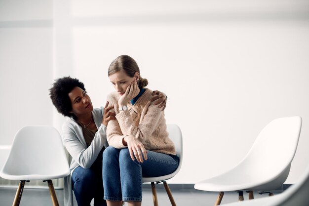 Mujer afroamericana cariñosa consolando a una mujer triste antes de la reunión de terapia de grupo