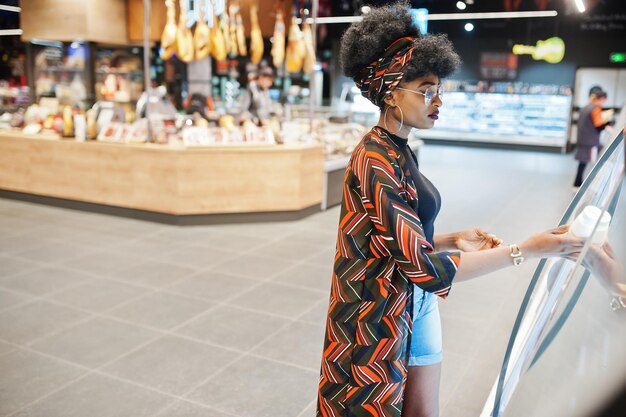 Mujer afroamericana elige una botella de yogur de la nevera en el supermercado