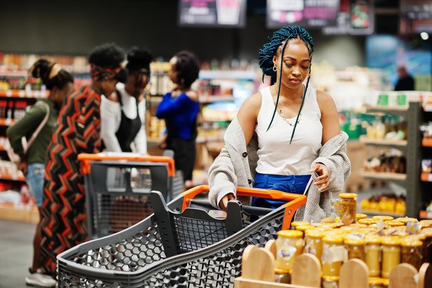 Mujer afroamericana elige tarro de miel en el supermercado contra sus amigos afro con carrito de compras