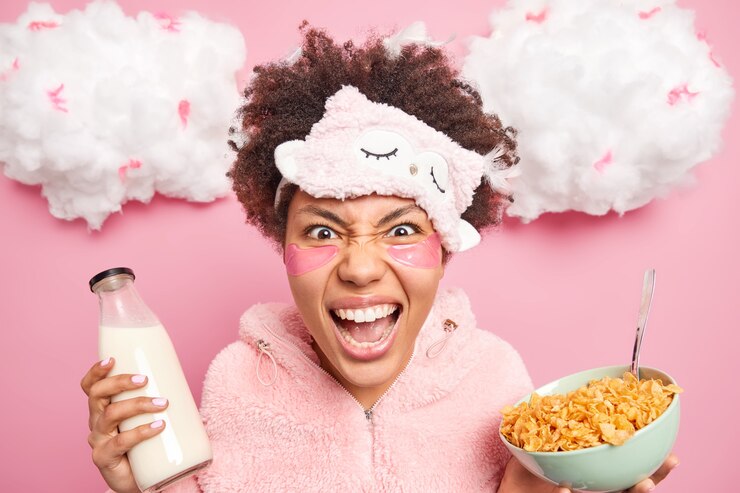Foto gratuito mujer afroamericana emocional loca grita enojada usa máscara de dormir suave y poses de pijama con tazón de copos de maíz y leche que se irrita cuando se despierta temprano en la mañana