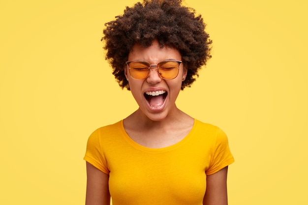 Mujer afroamericana emocional de piel oscura disgustada grita en voz alta, abre la boca