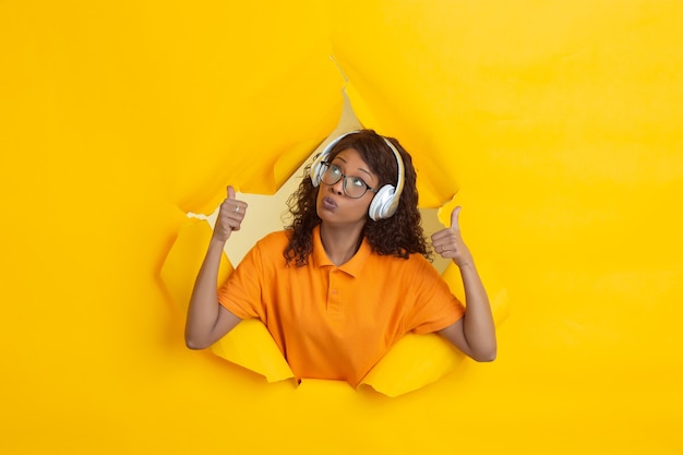 Mujer afroamericana escuchando música a través del orificio de la pared de papel amarillo