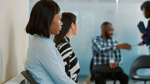 Mujer afroamericana esperando recibir cv y asistir a una entrevista de trabajo con el departamento de recursos humanos. Solicitante sentada en el vestíbulo de la oficina, preparándose para una cita de reunión sobre el empleo.