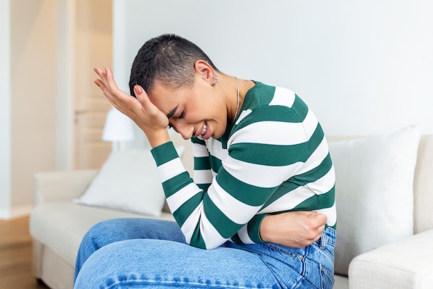 Mujer afroamericana en expresión dolorosa tomándose de la mano contra el vientre que sufre dolor menstrual acostada triste en la cama de su casa con calambres en el estómago en el concepto de salud femenina