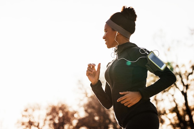 Foto gratuita mujer afroamericana feliz con auriculares corriendo en el parque