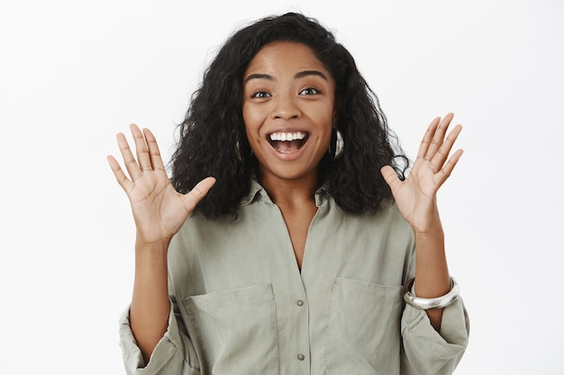 Mujer afroamericana feliz habladora emocionada con peinado rizado en traje de moda levantando las palmas gesticulando con alegría y sonriendo encantado