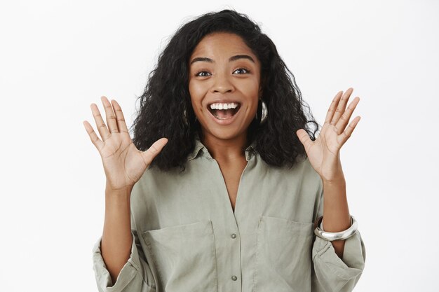 Mujer afroamericana feliz habladora emocionada con peinado rizado en traje de moda levantando las palmas gesticulando con alegría y sonriendo encantado