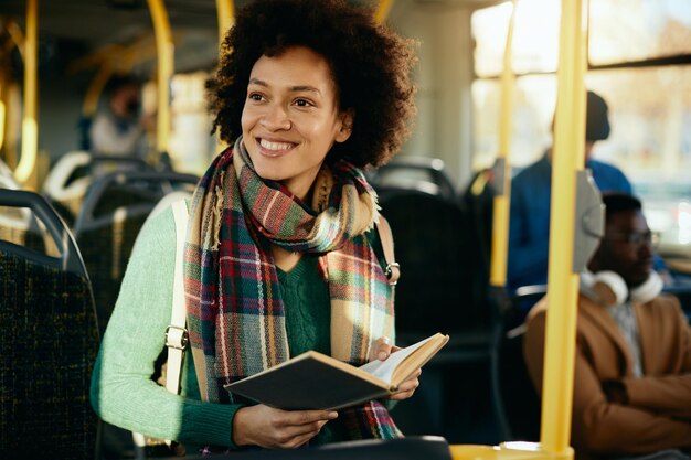Mujer afroamericana feliz leyendo un libro mientras viaja en autobús